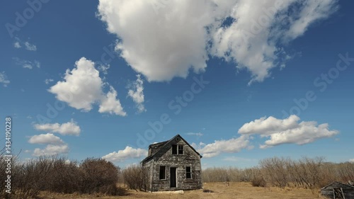 Time lapse of churning summer clouds in blue sky above an abandoned farmhouse
