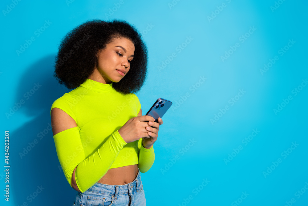 Young woman in neon top using smartphone against a blue background, embodying modern style, fashion, and vibrant youthfulness.