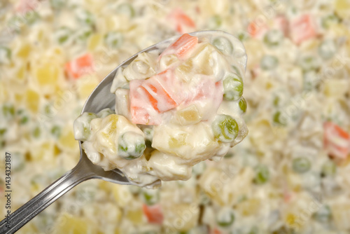 Obraz na płótnie A spoonful of creamy Croatian-style French salad with diced vegetables and mayonnaise is held over the remaining salad in a blurred background w salonie