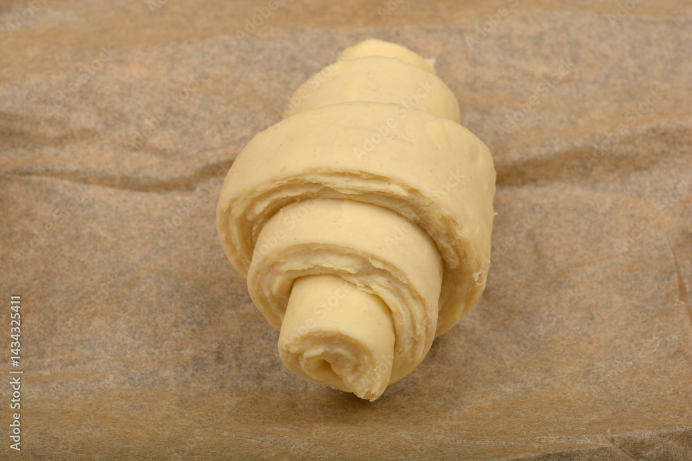 A single, unbaked croissant dough rests on a piece of parchment paper, ready for the oven