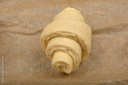 A single, unbaked croissant dough rests on a piece of parchment paper, ready for the oven