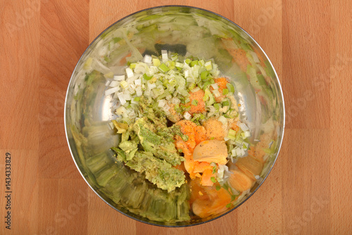 Obraz na płótnie A top-down view shows a stainless steel bowl containing mashed avocado, chopped onions, spices including garlic powder, and yolks, being prepared as a filling for deviled eggs, on a wooden surface w salonie