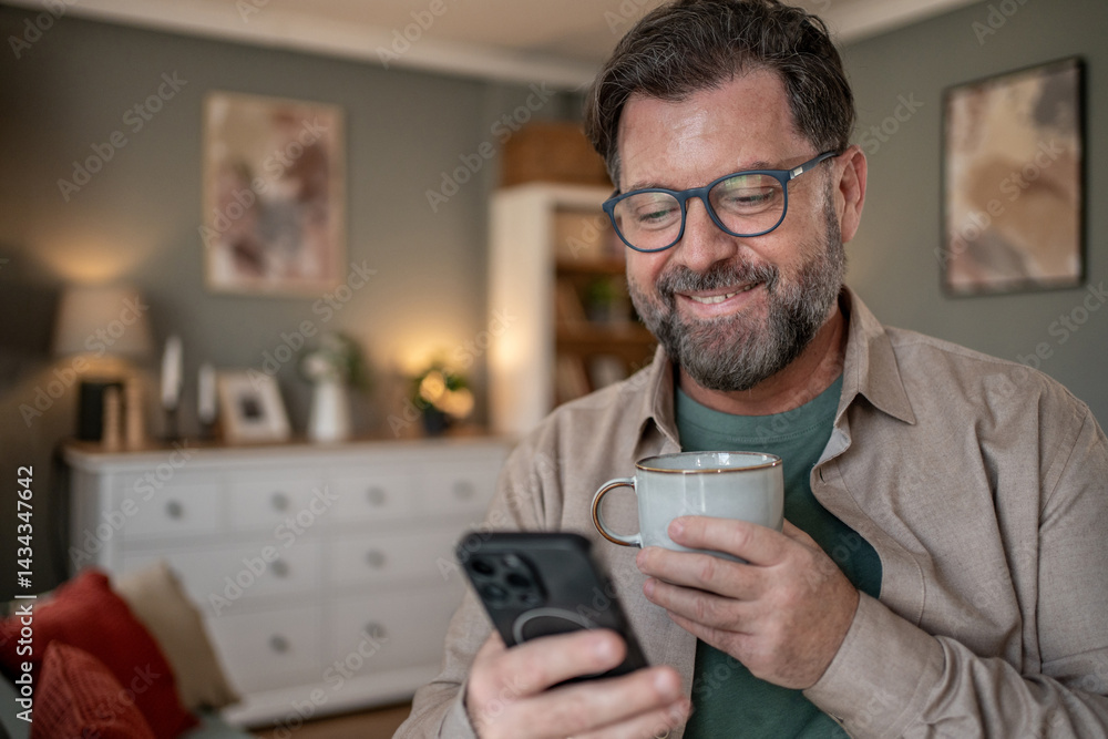 Smiling man using smartphone and drinking coffee at home Smiling man using smartphone and drinking coffee at home