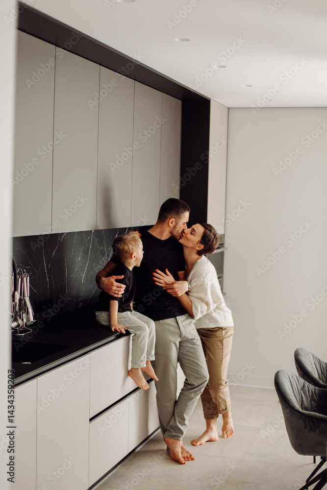 Obraz premium Parents kissing in kitchen while their son sits on the countertop
