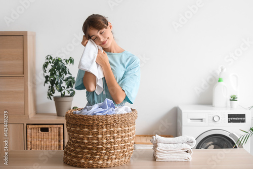 Happy young woman with clean towel in laundry room