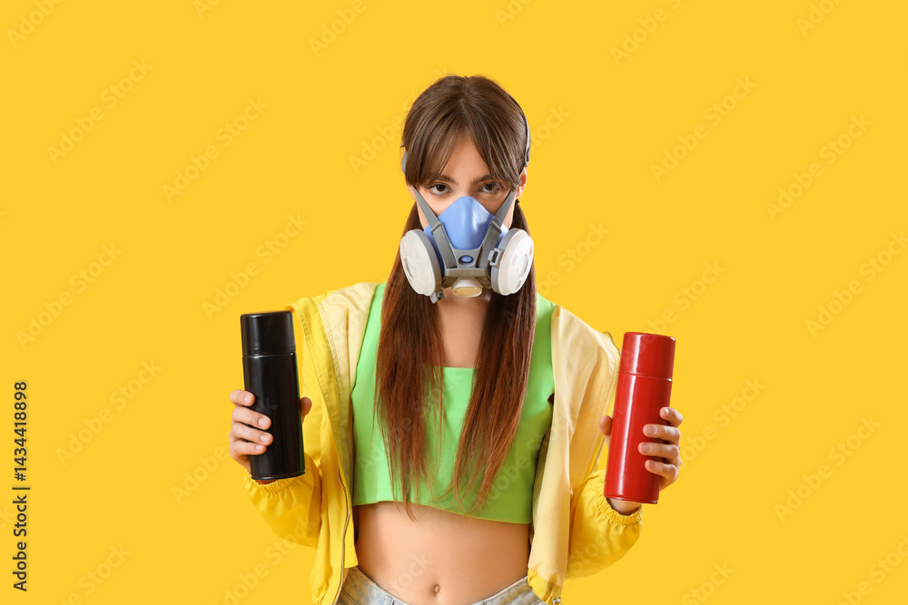 Young girl in respirator and with spray cans on yellow background