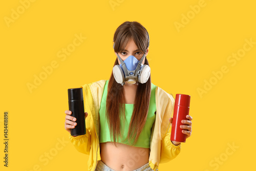 Obraz na płótnie Young girl in respirator and with spray cans on yellow background w salonie
