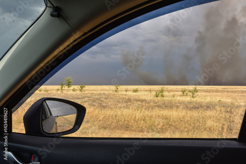 Car window shows a field with smoke in the distance