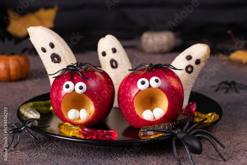 Spooky banana ghosts monsters and red apple monsters for Halloween party on brown background decorated with spiders and worms