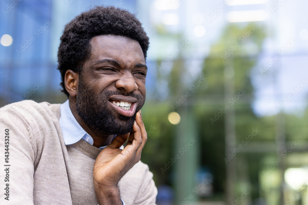 Man suffering from toothache. African American businessman sitting on a bench outside an office building and holding his hand over his gap, inflammation of the gums.