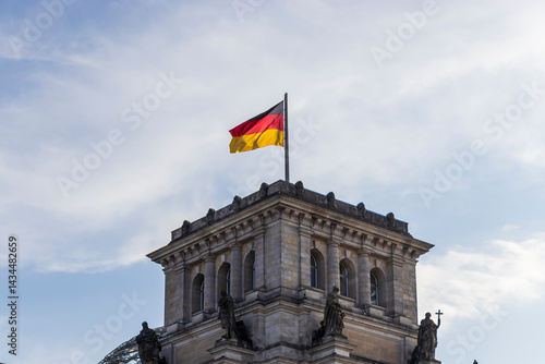 The German flag waves proudly atop the Reichstag building in Berlin under a bright blue sky. This iconic structure symbolizes history, democracy, and national pride.