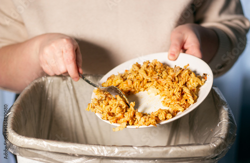 Woman holding food plate and throwing away food leftovers using spoon into garbage bin trash. Compost from leftover food. Stop Food Waste Day