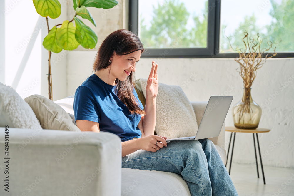 Young woman looking at laptop screen talking having video call sitting on couch at home