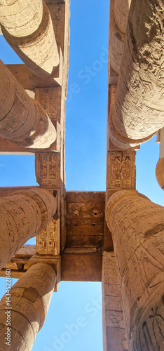 Looking up at ancient stone columns with hieroglyphs in Karnak Temple, Luxor, Egypt – monumental pharaonic architecture under clear blue sky