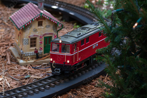 Miniature electric toy train passing through a model plastic Christmas village with Christmas trees on a bed a mulch