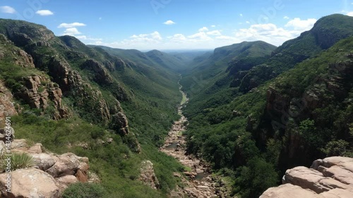 Picturesque aerial view of lush green valley with rocky mountain cliffs under a partly cloudy sky offering an outdoor landscape experience