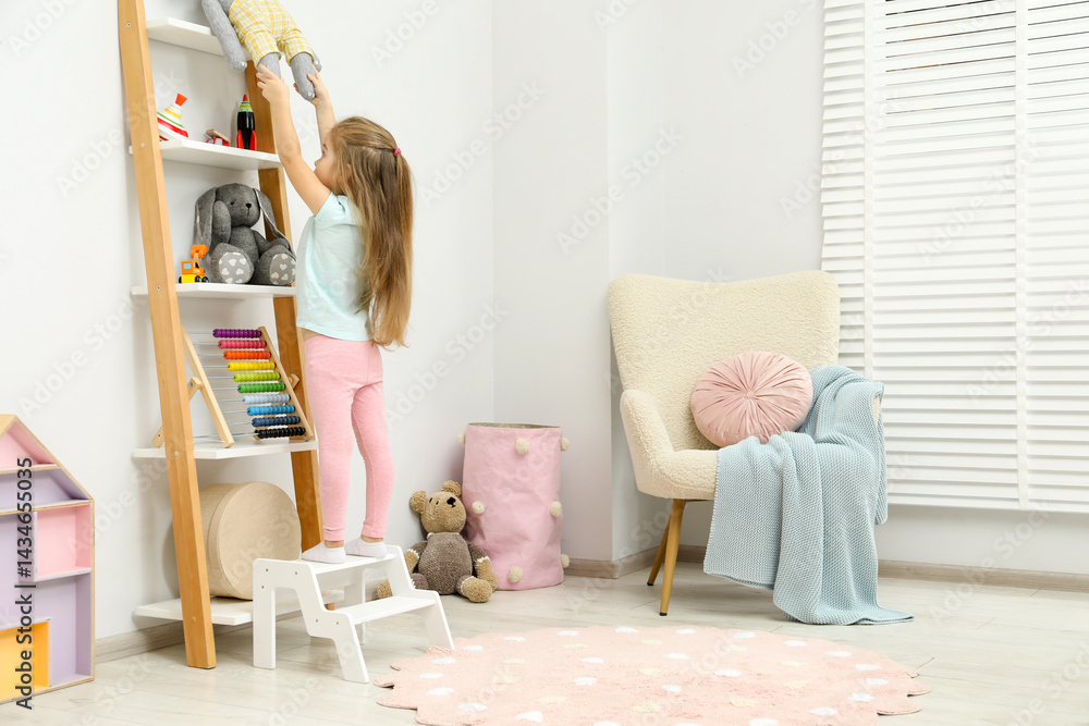 Little girl standing on step stool and reaching for toys on shelf indoors. Space for text