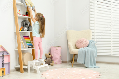 Obraz na płótnie Little girl standing on step stool and reaching for toys on shelf indoors. Space for text w salonie