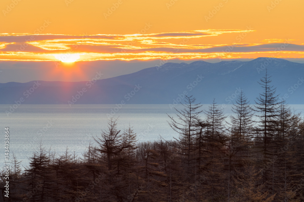 Morning landscape. Sunrise over the sea bay. Larch forest on the coast. Rising sun over the mountains. Autumn season. Nature of Siberia and the Russian Far East. Travel in the Magadan region. Russia.