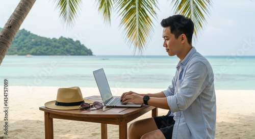 Fototapeta Naklejka Na Ścianę i Meble -  Man works on laptop at beach table with ocean and island background.