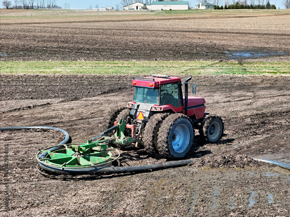 Obraz premium Red tractor using a liquid manure hose mover to assist in field opperations.