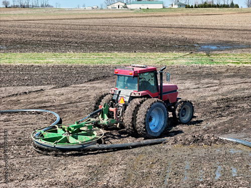 Red tractor using a liquid manure hose mover to assist in field opperations.