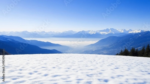 Snowy foreground overlooks valley & distant mountains under a clear blue sky