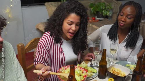 Young Latin woman serves herself salad and chats with her black friend at an outdoor evening gathering