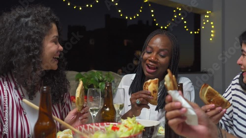 At a night dinner, young black woman talks to her Latin friends while eating empanadas