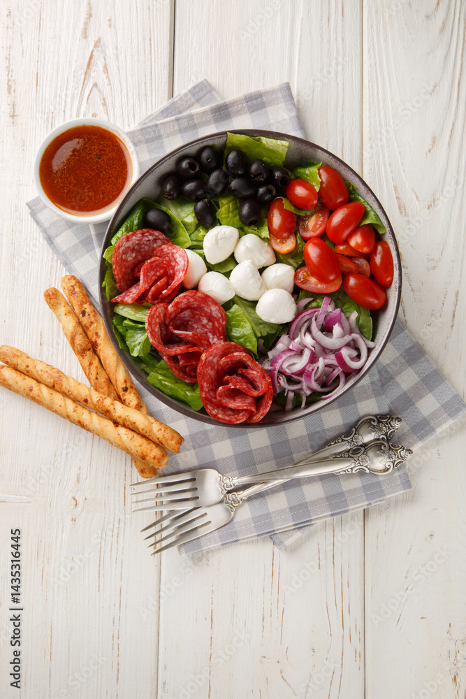 Pizza salad tosses mix of romaine lettuce, sausages, mozzarella, black olives and red onion in a fresh, grated tomato vinaigrette closeup on the plate on the wooden table. Vertical top view from above
