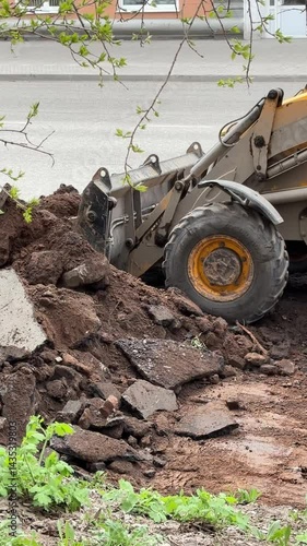 Excavator shoveling earth by roadside for urban construction project