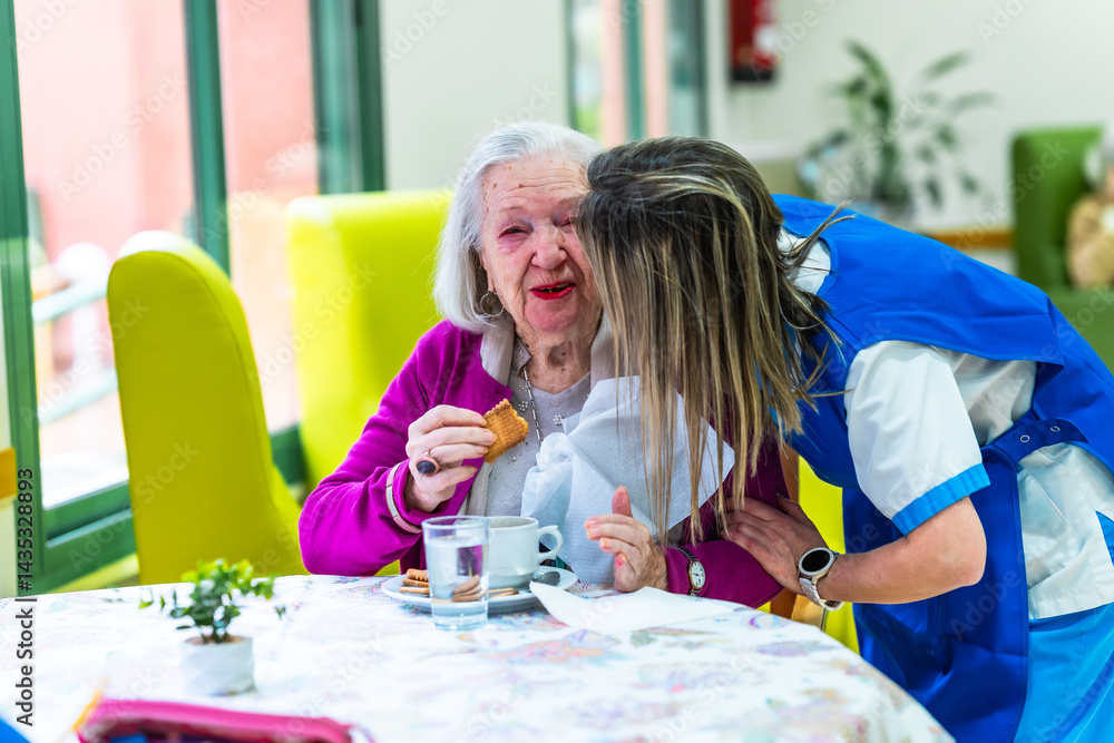 Nurse assisting elderly woman eating a biscuit in nursing home