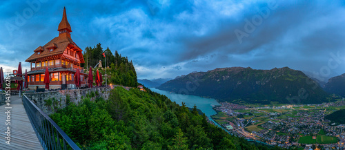 Fotografie Panorama of Lake Brienz, Interlaken, and the surrounding Swiss Alps from Harder Kulm in Switzerland, with dramatic clouds and lush green valleys