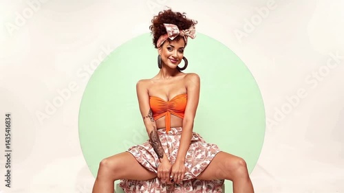 Woman is sitting on a green box with a pink skirt on. She is wearing a red top and has a pink headband