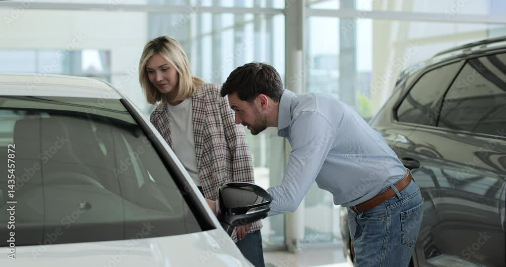 Attractive young couple discussing chosen auto in automobile showroom. Concept of car shopping, buying, and dealership. Attractive young couple discussing chosen auto in automobile showroom. Concept of car shopping, buying, and dealership.