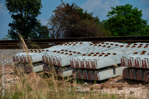 Railway Sleepers: An organized arrangement of sturdy railway sleepers lies neatly beside a set of railroad tracks, framed by natural surroundings. Evoking industrial infrastructure.