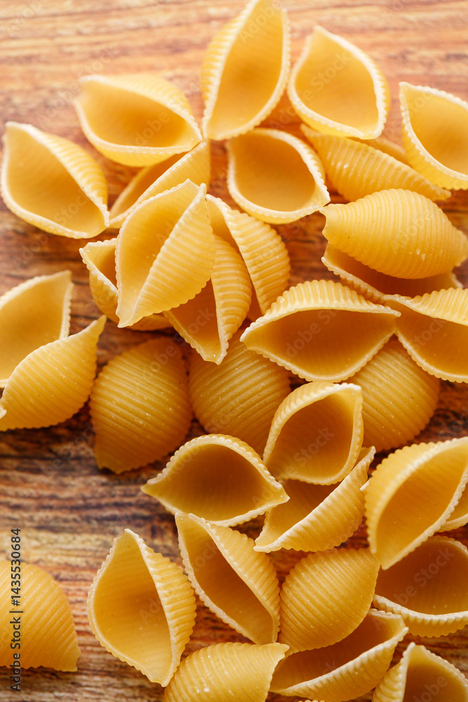 Raw uncooked dried Conchiglie shell pasta. Italian seashells pasta on wooden background. Raw uncooked dried Conchiglie shell pasta. Italian seashells pasta on wooden background.