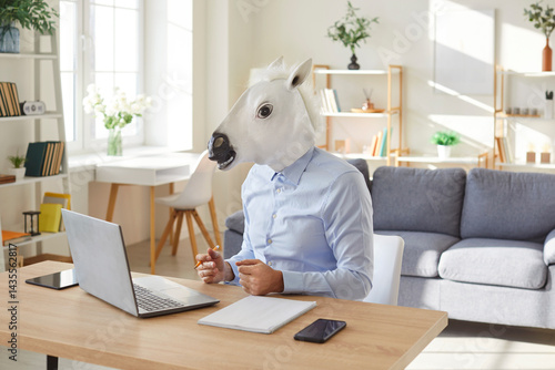 Funny extravagant happy man wearing donkey, horse head working online at desk to enjoy showing impressive achievements, successful deal, cute amuse guy playing, business worker at computer working