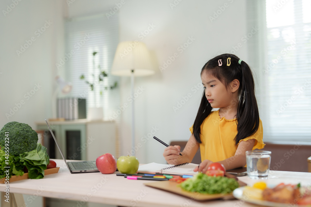 Young girl taking notes in her notebook while looking at her laptop, learning about healthy eating habits, with various fruits and vegetables on the table beside her notebook Young girl taking notes in her notebook while looking at her laptop, learning about healthy eating habits, with various fruits and vegetables on the table beside her notebook