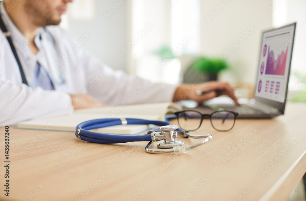 Stethoscope lying on the table near a doctor or nurse working online with a laptop in a hospital or clinic office. Professional medical equipment, healthcare expertise, and quality care.