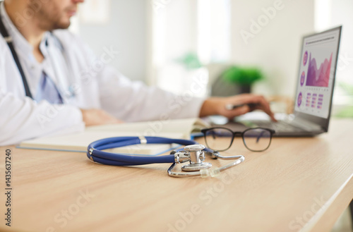 Obraz na płótnie Stethoscope lying on the table near a doctor or nurse working online with a laptop in a hospital or clinic office. Professional medical equipment, healthcare expertise, and quality care. w salonie