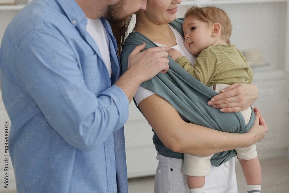 Fototapeta premium Parents with their baby indoors. Mother holding her child in sling at home, closeup