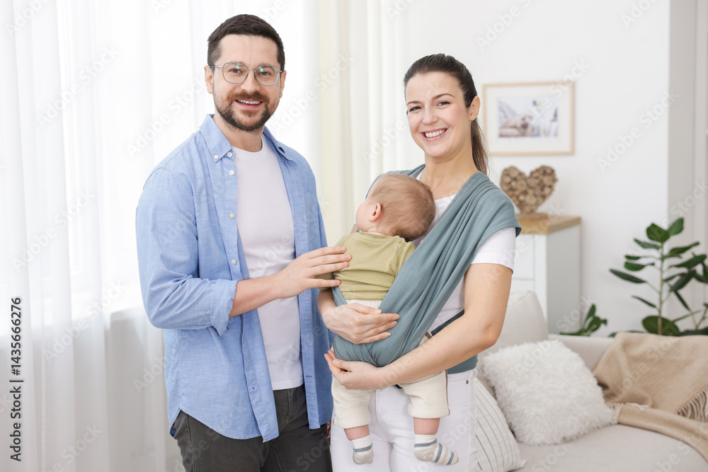 Fototapeta premium Portrait of happy family indoors. Mother holding her child in sling (baby carrier) at home