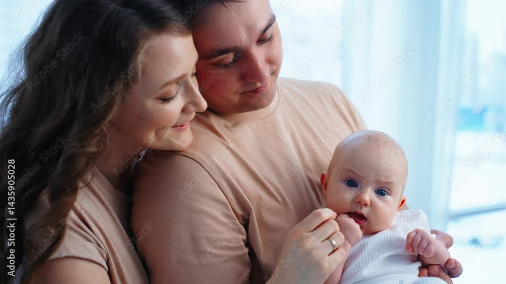A happy family is gathered together in a well-lit room, embracing a moment of love and connection. The parents, dressed in matching outfits, share gentle gazes while holding their baby. The baby A happy family is gathered together in a well-lit room, embracing a moment of love and connection. The parents, dressed in matching outfits, share gentle gazes while holding their baby. The baby