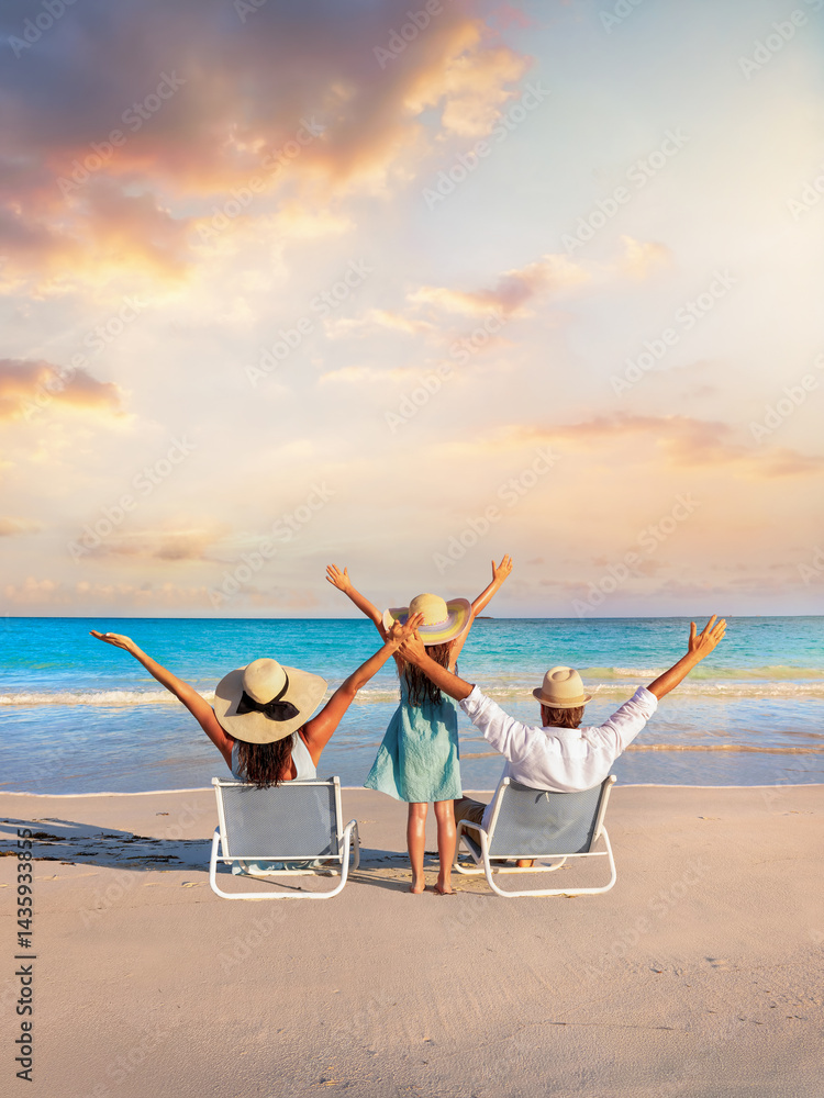 A happy family on summer holidays sits on a tropical beach and enjoys together the beautiful sunset