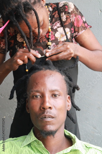 African Man with dreadlocks in a hair salon plaited by a young African lady