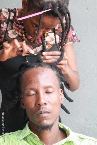 African Man with dreadlocks in a hair salon plaited by a young African lady