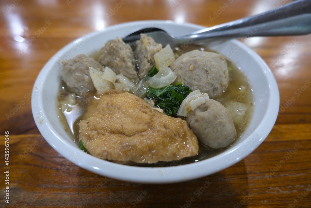 Close-up of a traditional Indonesian meatball soup or bakso served in a white bowl with tofu, vegetables, and savory broth Close-up of a traditional Indonesian meatball soup or bakso served in a white bowl with tofu, vegetables, and savory broth