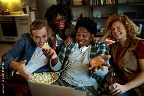 Group of friends drinking beer eating pizza and watching movie on laptop at home party