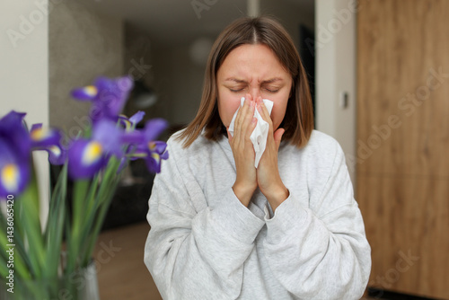 Seasonal allergy. Close up face of allergic young woman uses paper tissues from runny nose, sneezes from flowers pollen at home. Girl with close eyes with flu, itching or cough, allergy rhinitis